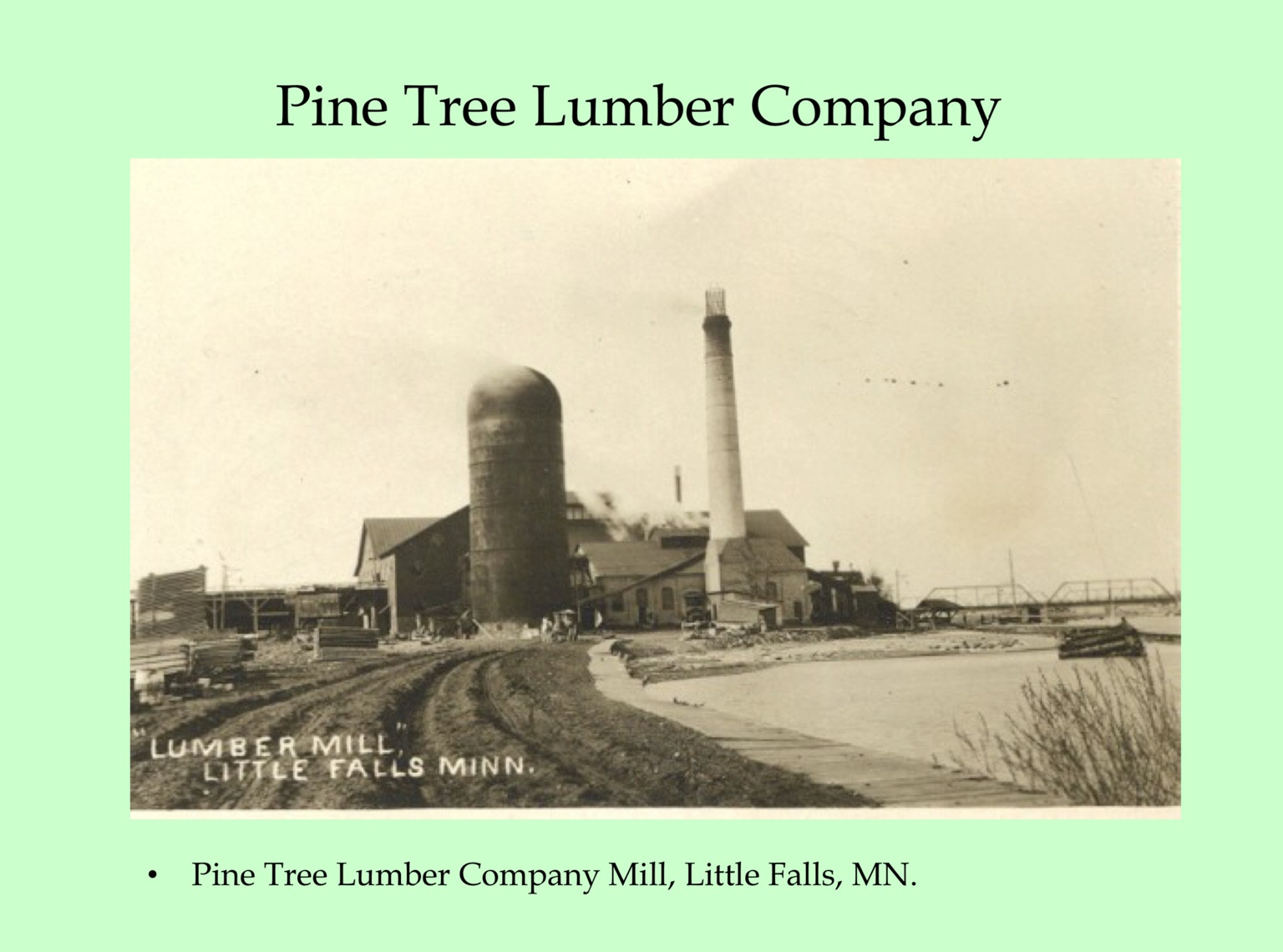 Lumber mill buildings, stacks and a riverside landing at Little Falls.