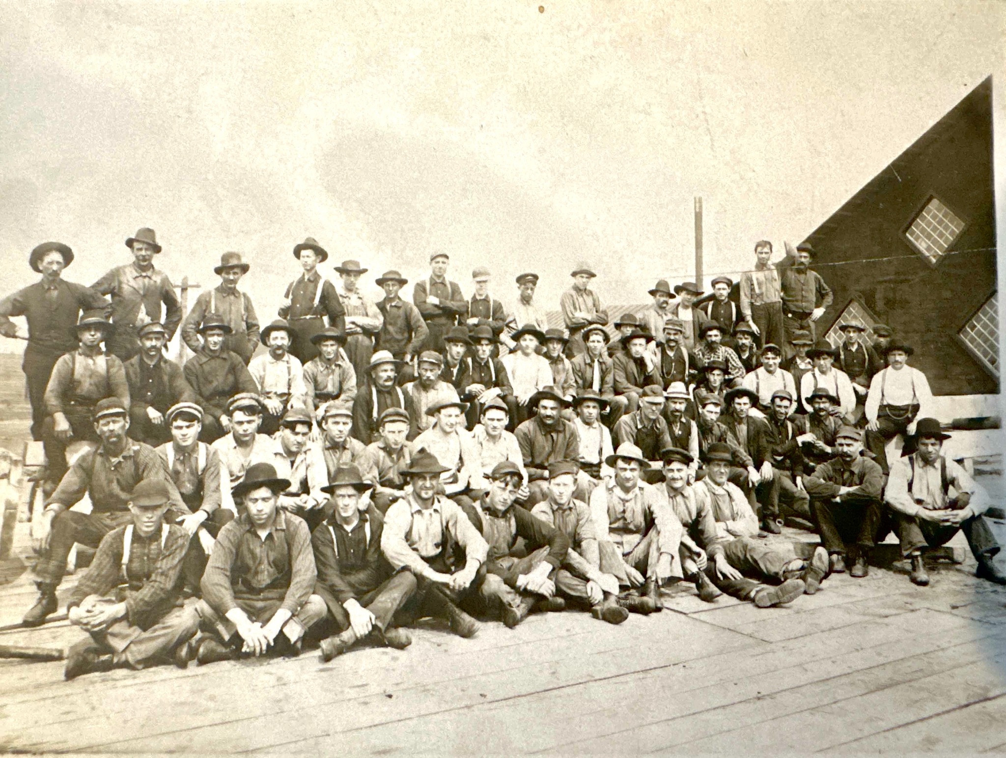 Pine Tree Company workers posed in rows outside a wooden building; Gustaf is not individually identified.