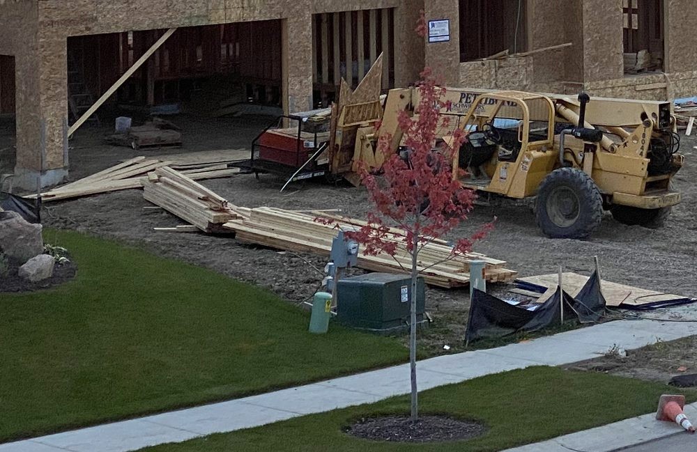 Stacks of lumber beside a partially framed building and a telehandler.