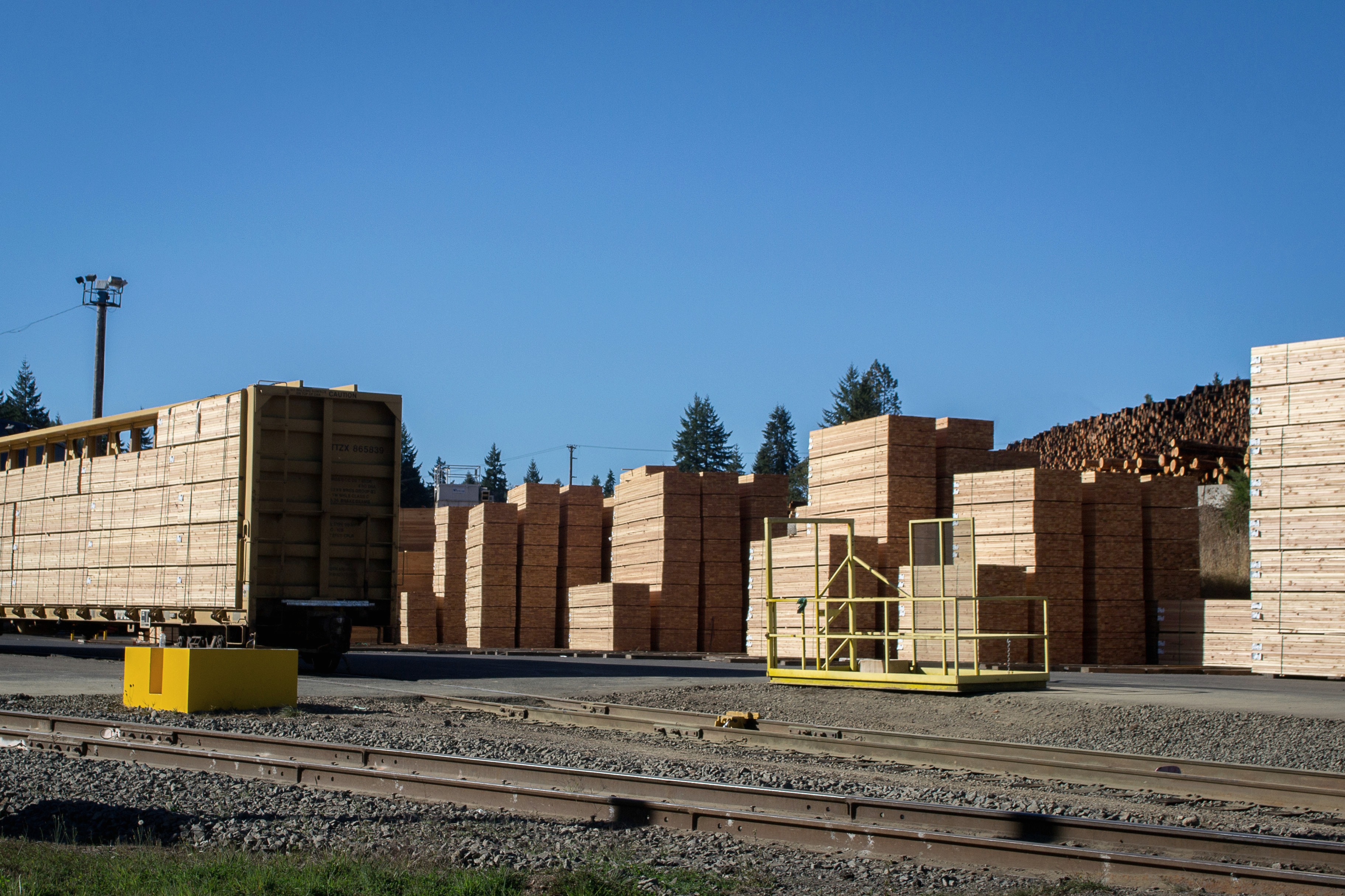 Stacks of sawn lumber and logs at a sawmill yard.