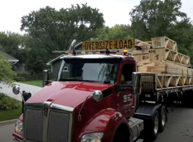 A red truck carrying bundled timber trusses on a flatbed.